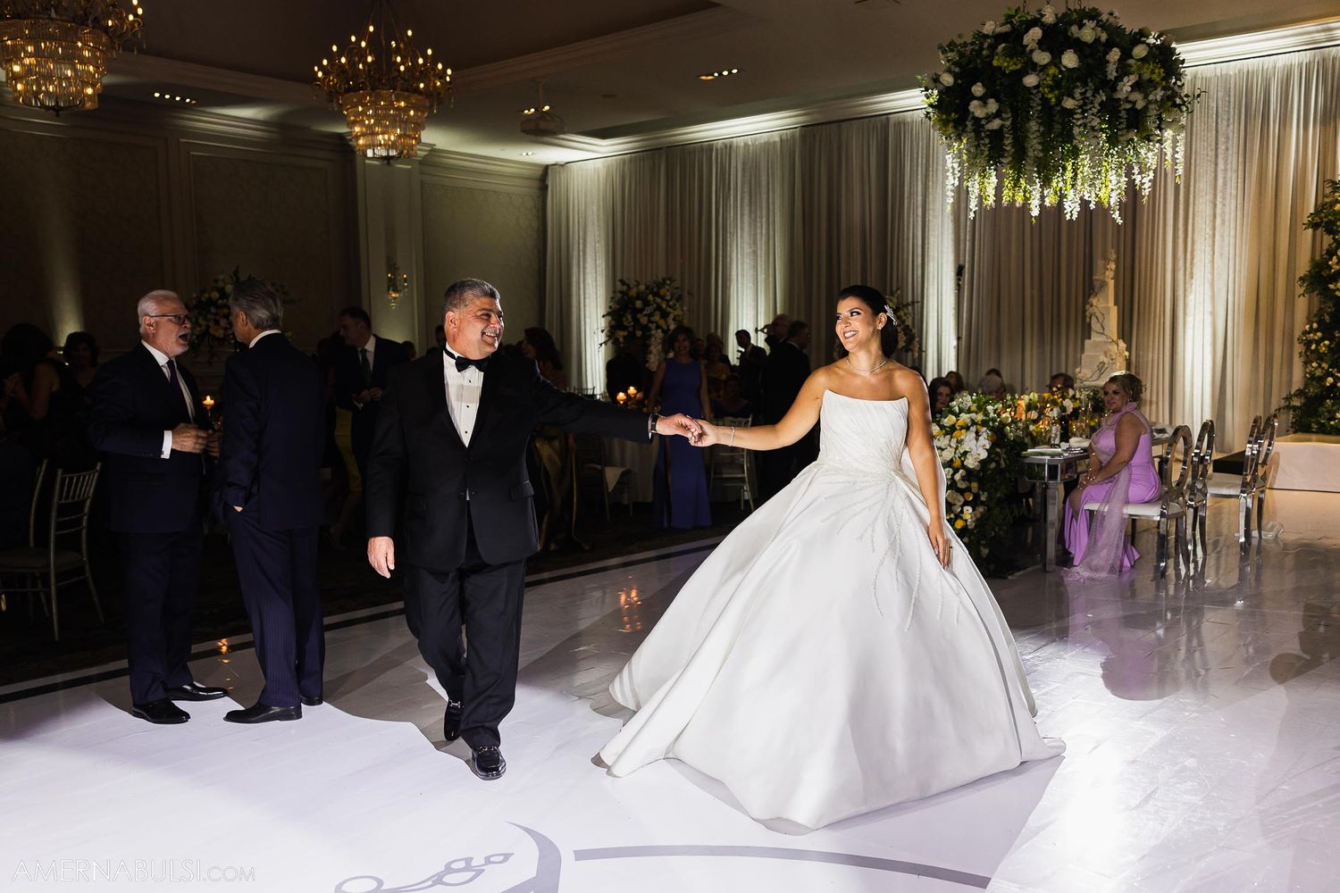 Couple dancing on misty white dance floor under elegant ballroom chandeliers.