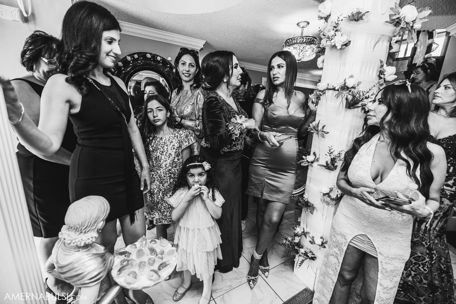 Black and white photo of wedding guests gathered in celebration at indoor reception.