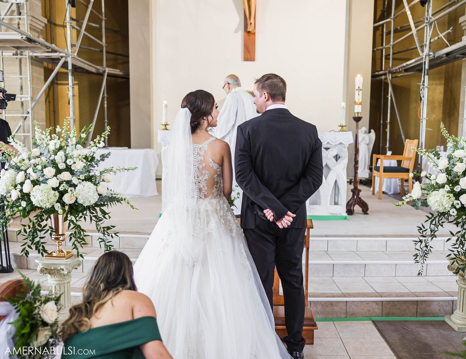 Back view of a couple standing at altar with white floral arrangements and wedding decorations.
