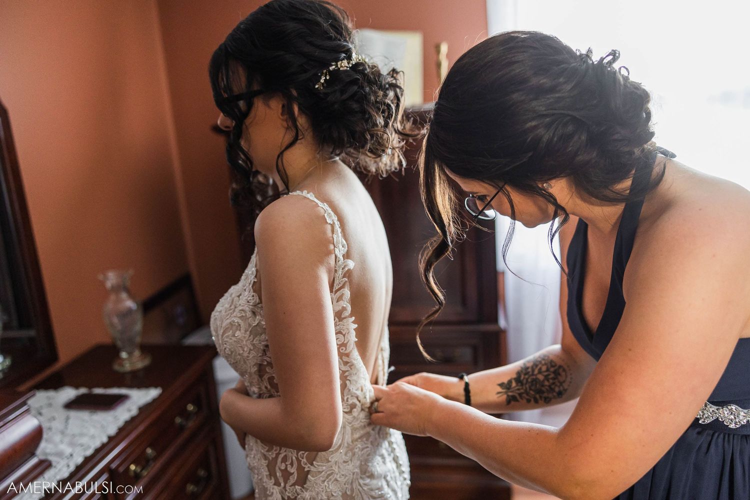 A wedding dress being fastened by helping hands during bridal preparation.