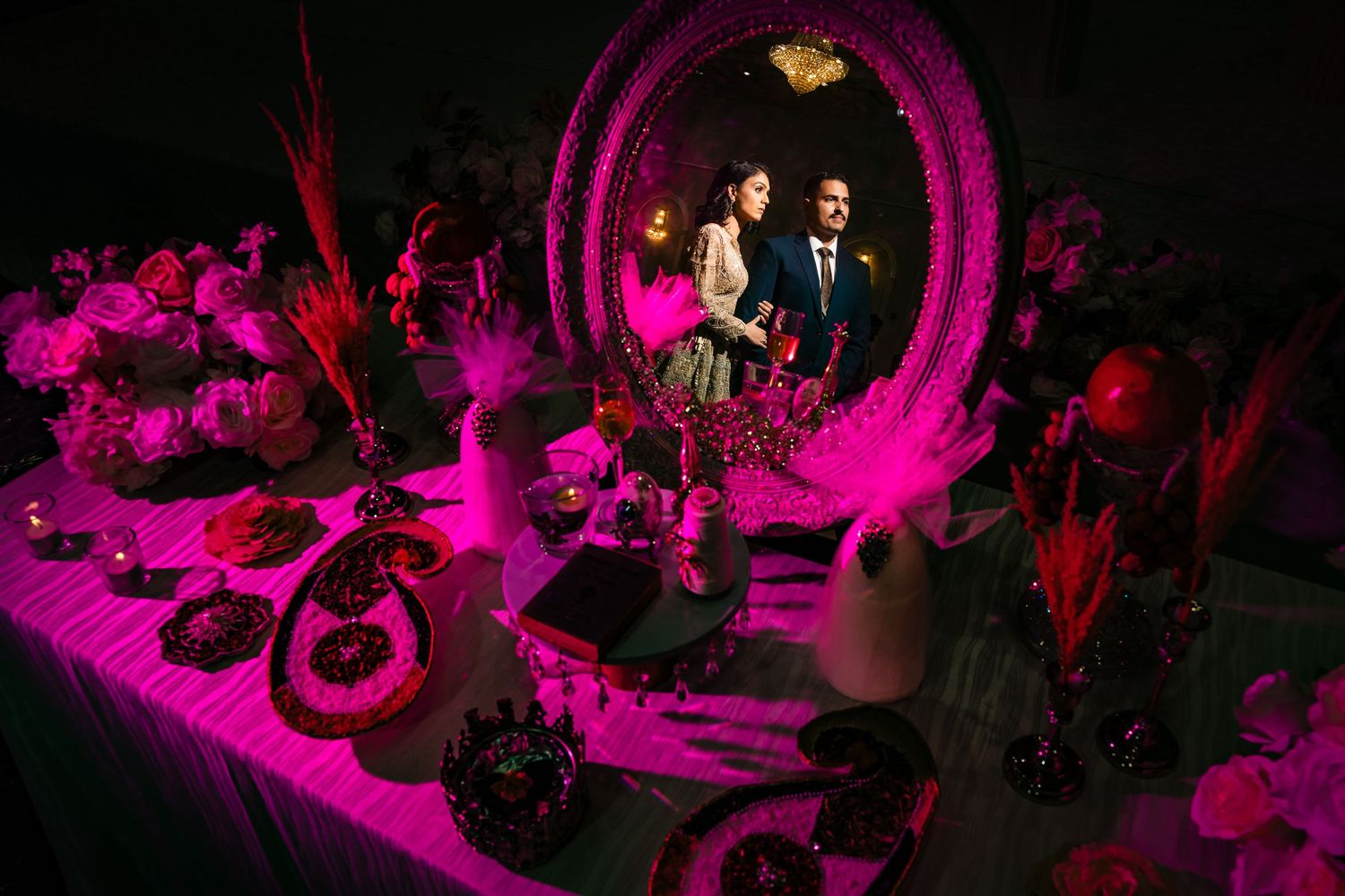 Wedding dessert table illuminated by dramatic pink lighting with mirror display.