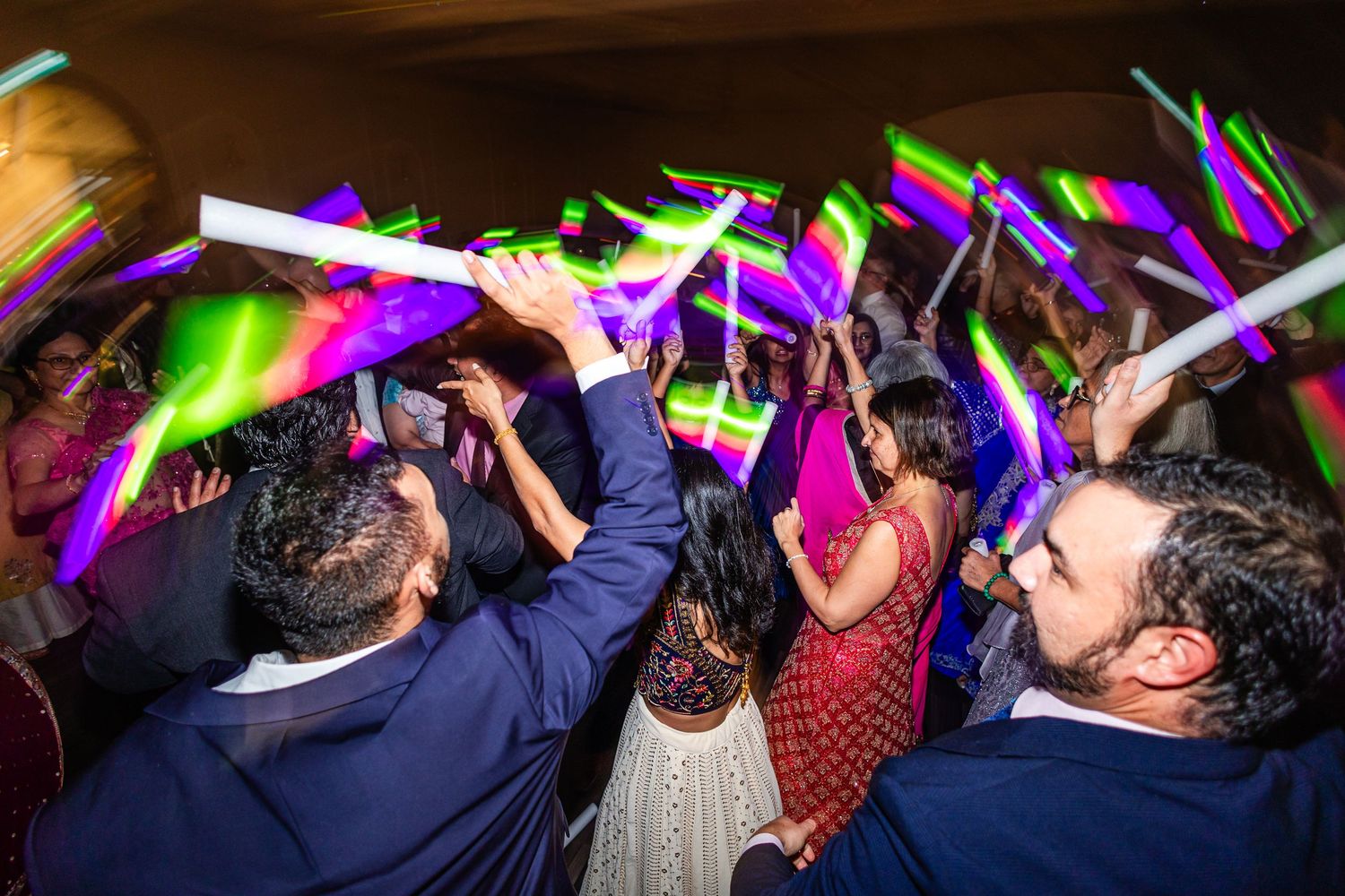 Party crowd waves glowing neon light sticks in the air during a dark nightclub celebration.