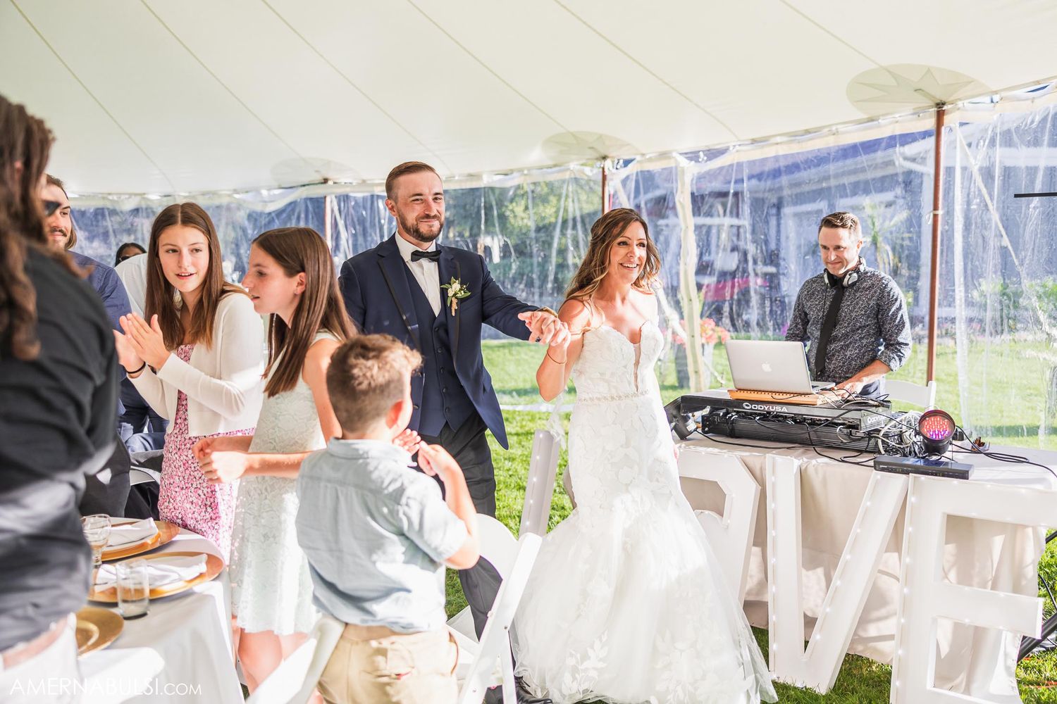 Festive wedding reception scene with guests celebrating under white tent.
