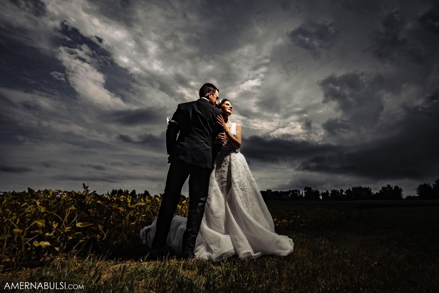 Dramatic sunset wedding portrait with stormy clouds behind couple in field.
