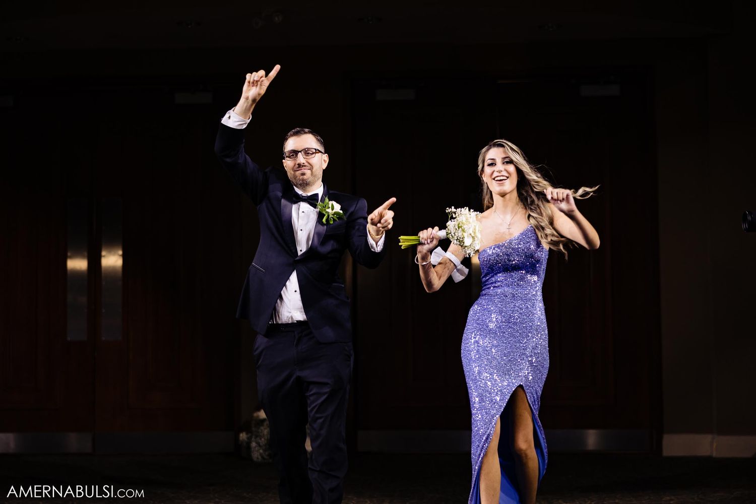 Celebratory moment of couple in formal wear raising arms in joy.