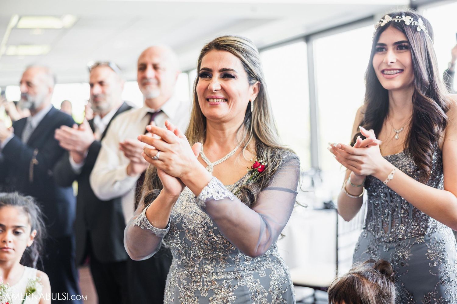 Wedding guests in sparkly dresses clap along during reception celebration.