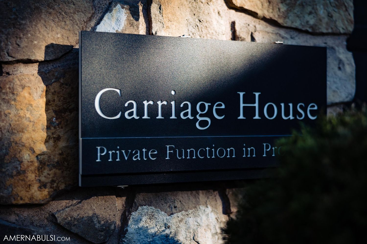 Black sign reading 'Carriage House Private Function' mounted on stone wall.