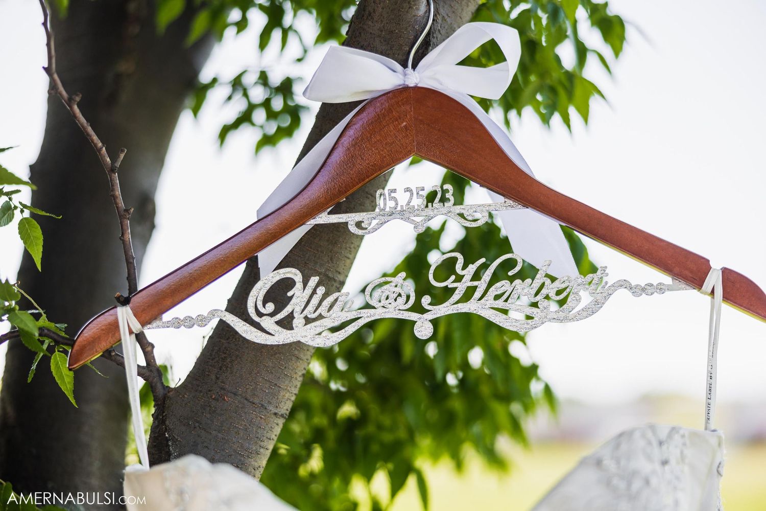 Custom wooden wedding hanger with decorative text displayed against green leaves.