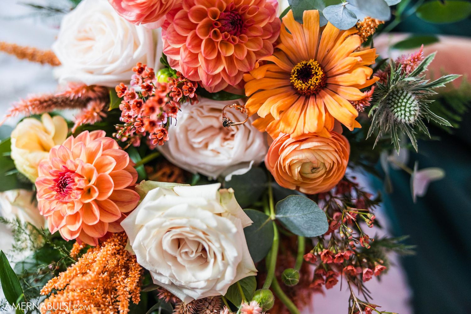 Stunning bridal bouquet featuring coral dahlias, peachy roses, and orange flowers with greenery.