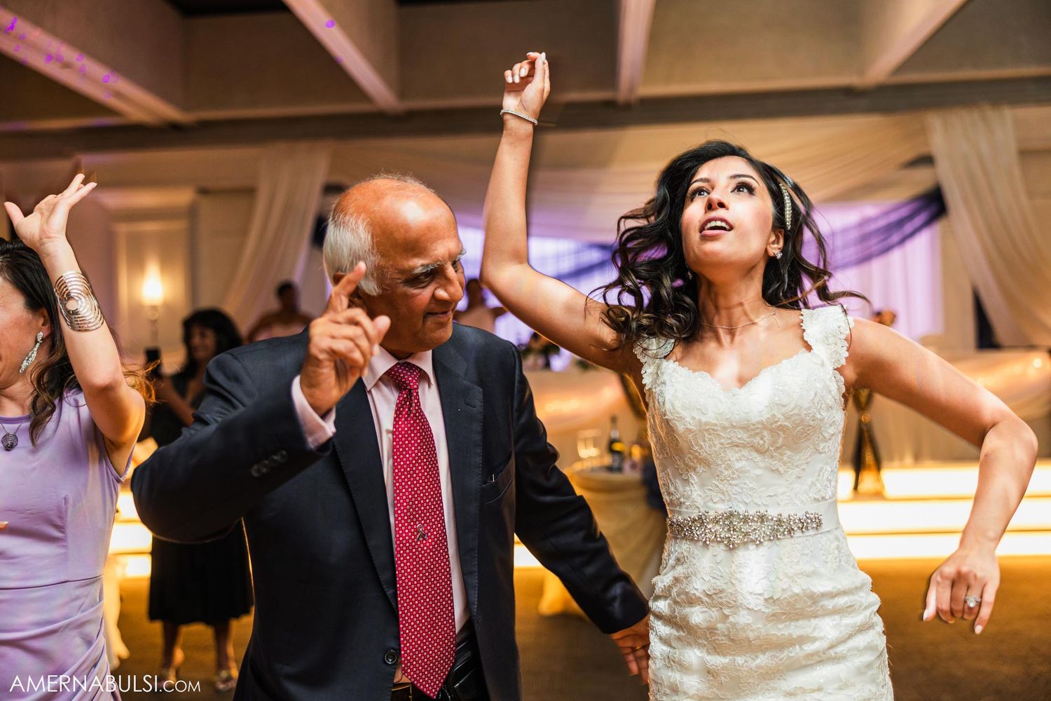 Joyful celebration dancing at an indoor wedding reception with decorative drapes.