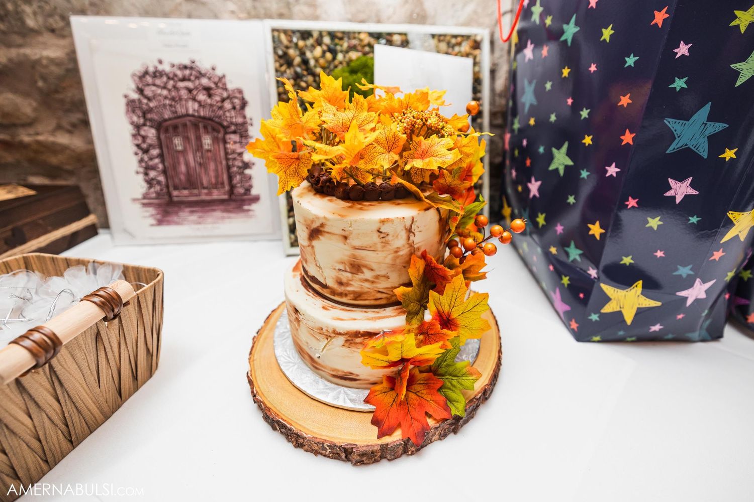 Rustic wedding cake decorated with autumn flowers and leaves on wood slice stand.