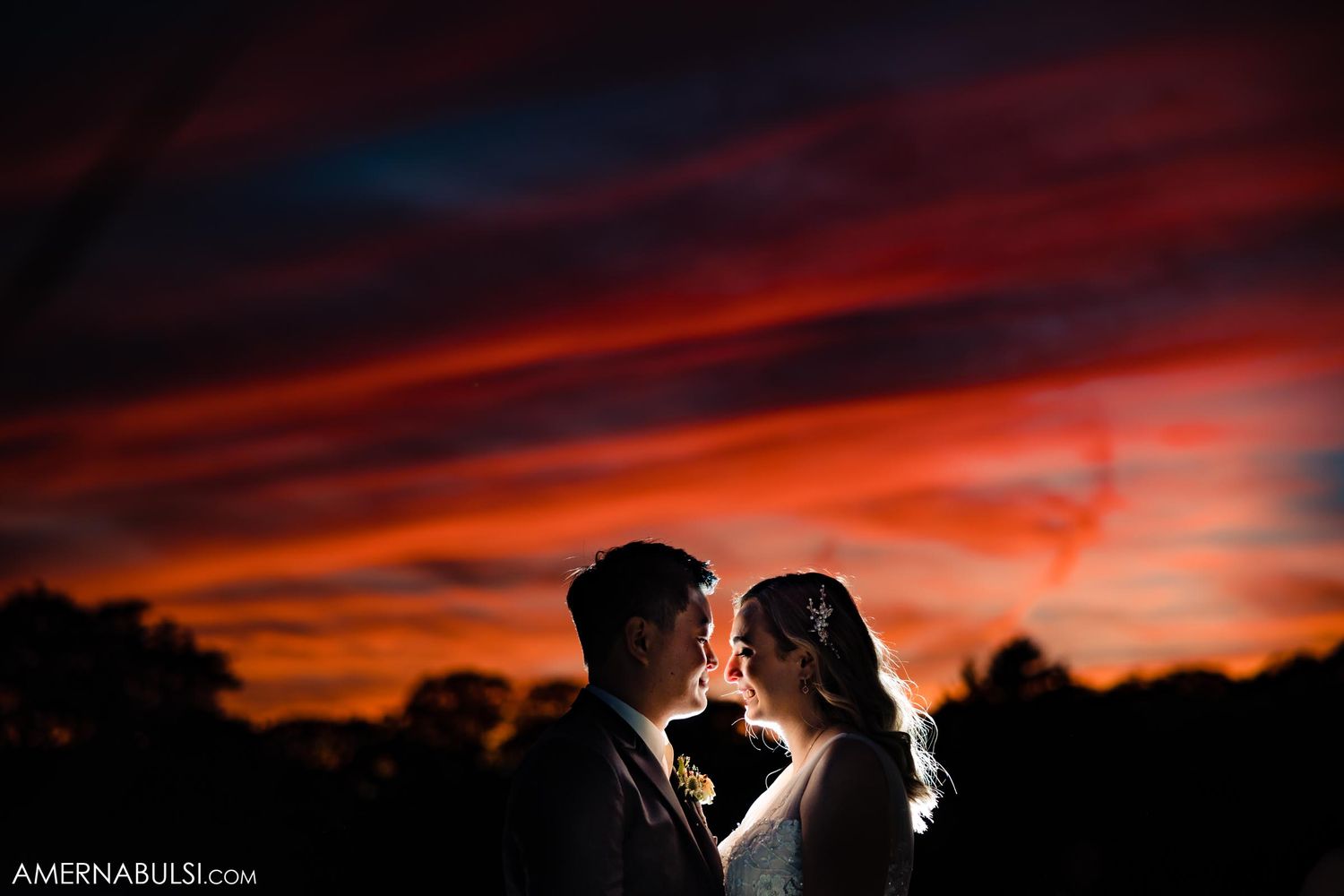 A couple shares an intimate moment against a dramatic red and orange sunset sky.