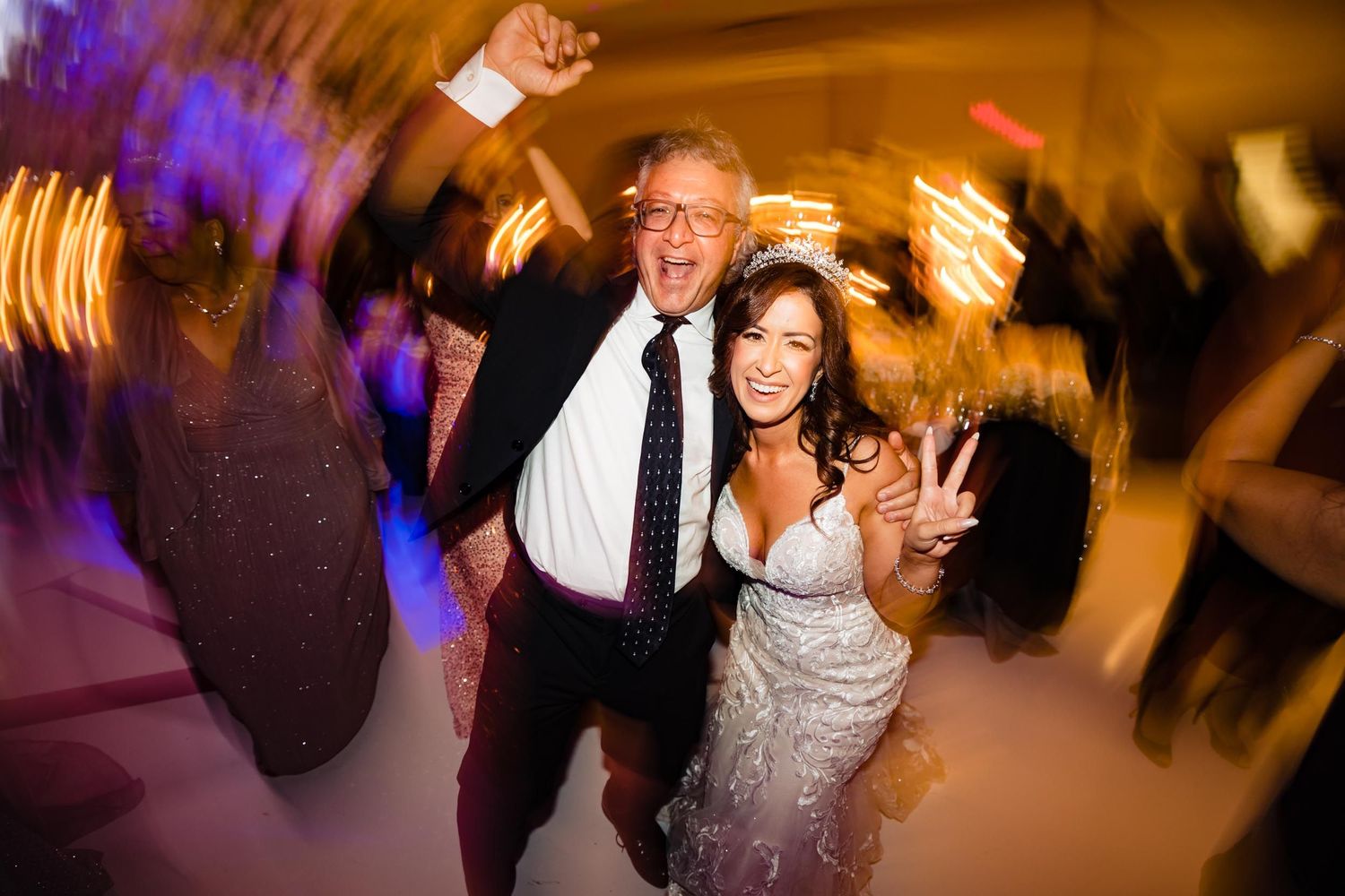 Energetic dancing and celebration in motion at wedding reception with blurred lights.