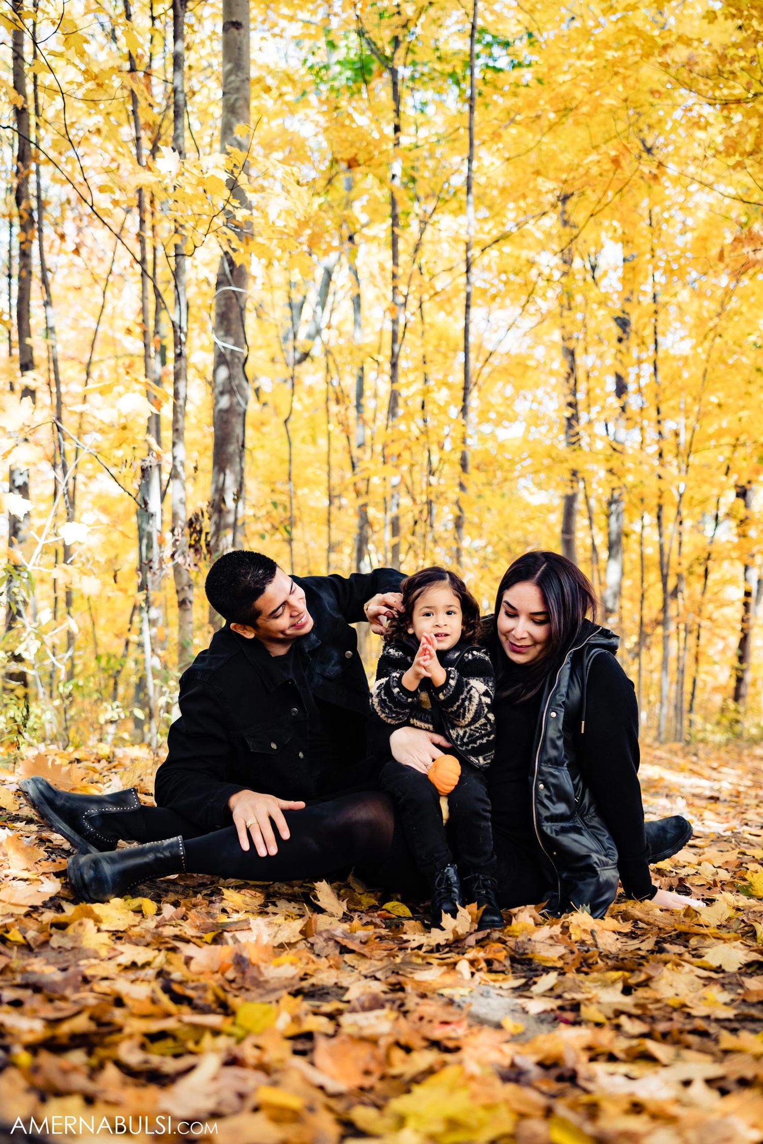 Family sitting together on fallen leaves in golden autumn forest.