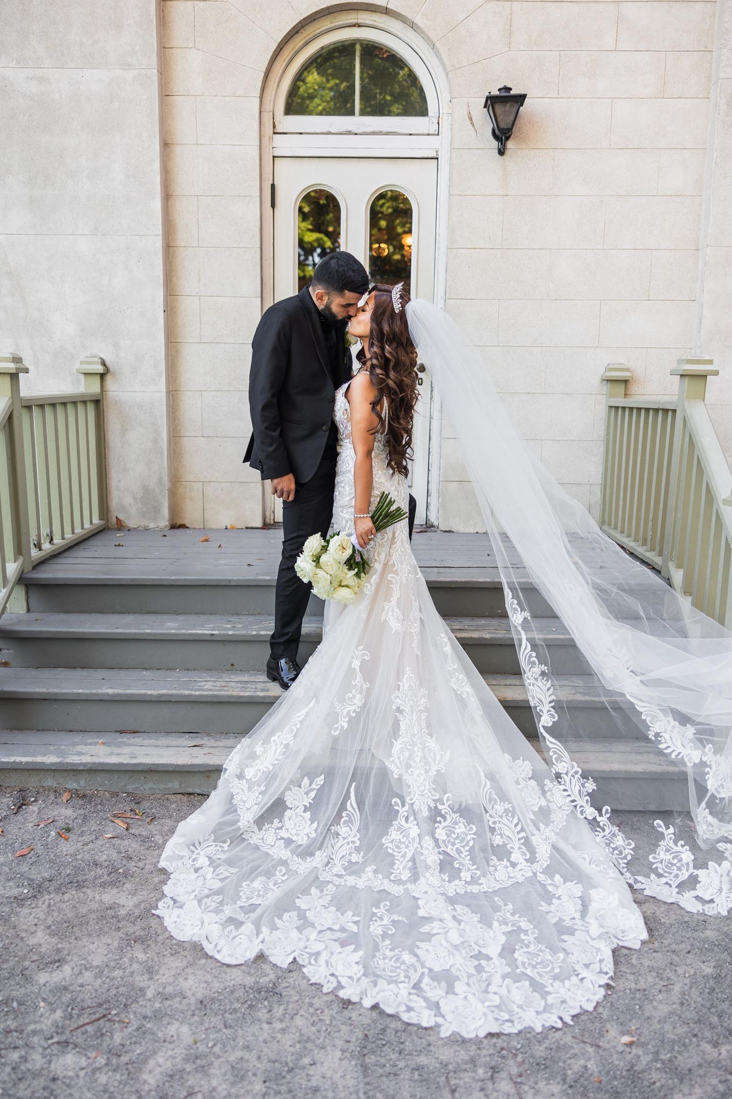 Bride's lace wedding dress train and veil flow beautifully on mansion steps.