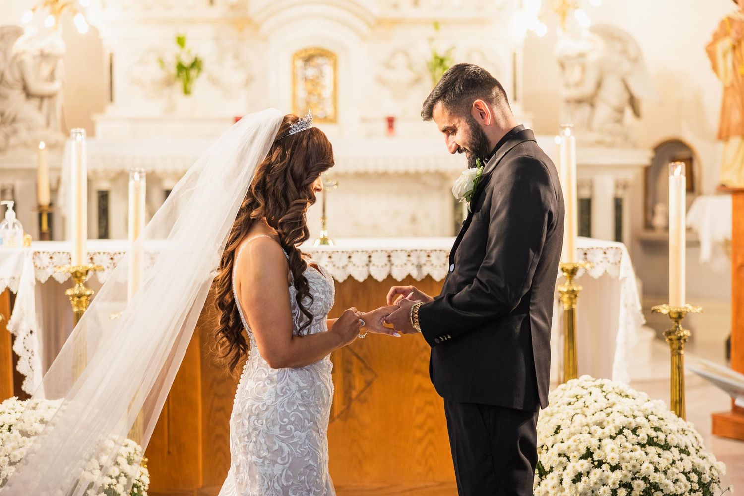 Wedding ceremony moment at ornate church altar with white floral decorations.