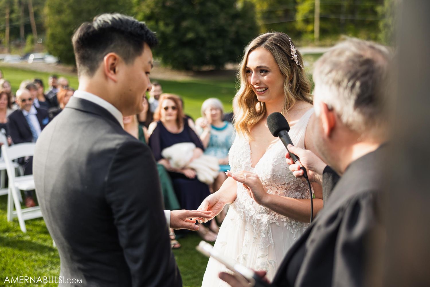 Wedding ceremony exchange of rings outdoors on golf course with guests watching.