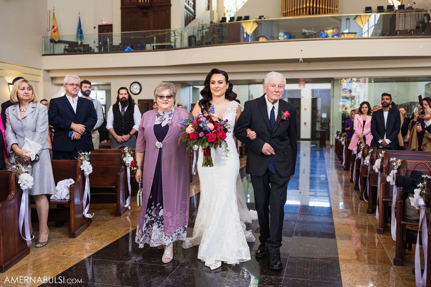 Wedding processional down church aisle with stained glass windows and wooden pews.