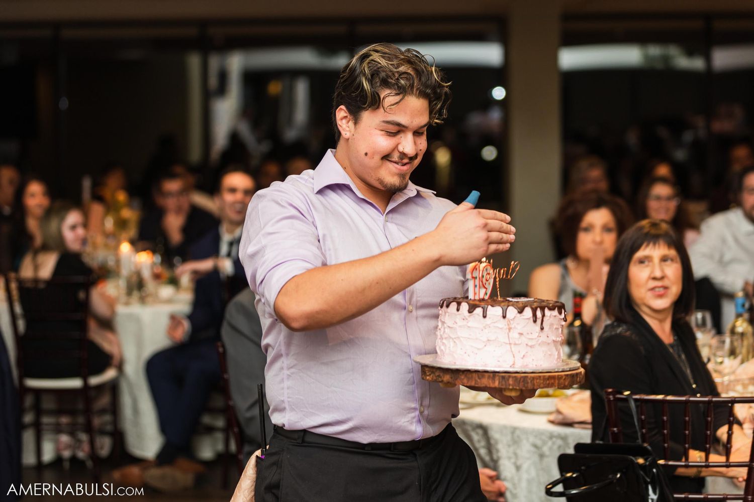 Guest at wedding reception holding and preparing to serve a decorated birthday cake.