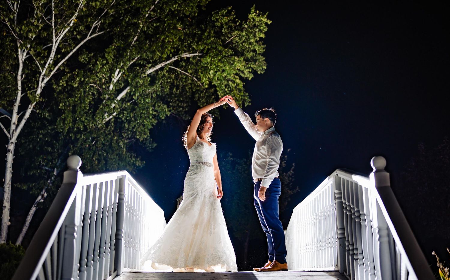A romantic nighttime dance pose on a white bridge illuminated against a dark sky.