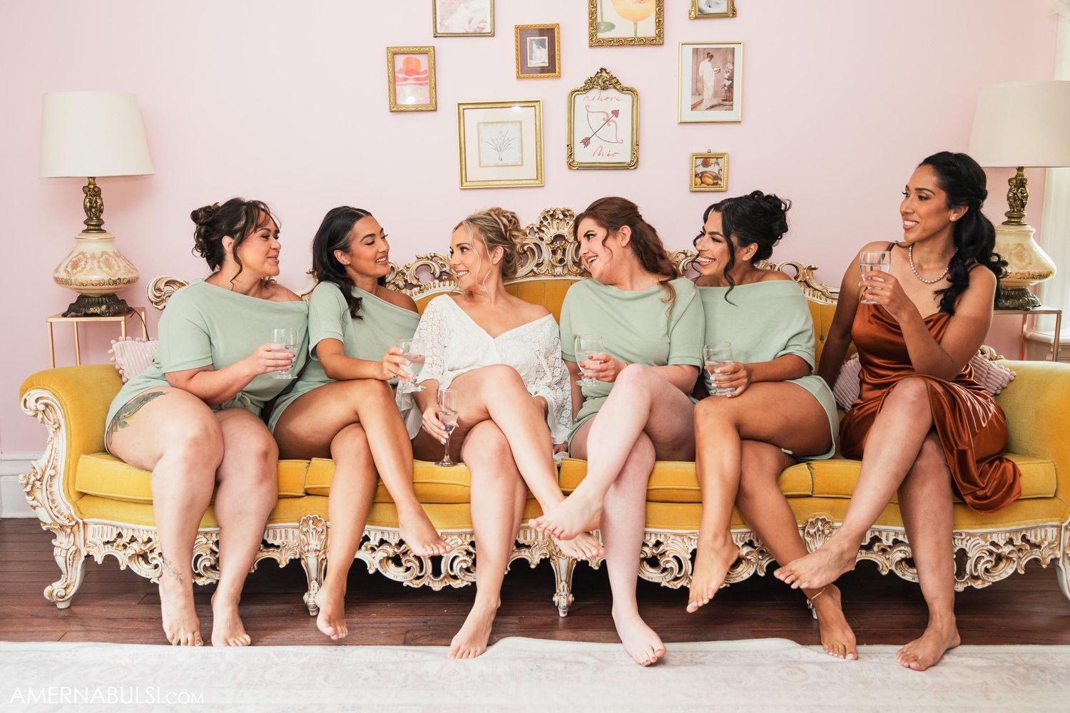 Bridal party in mint green and copper dresses seated together on vintage yellow couch.
