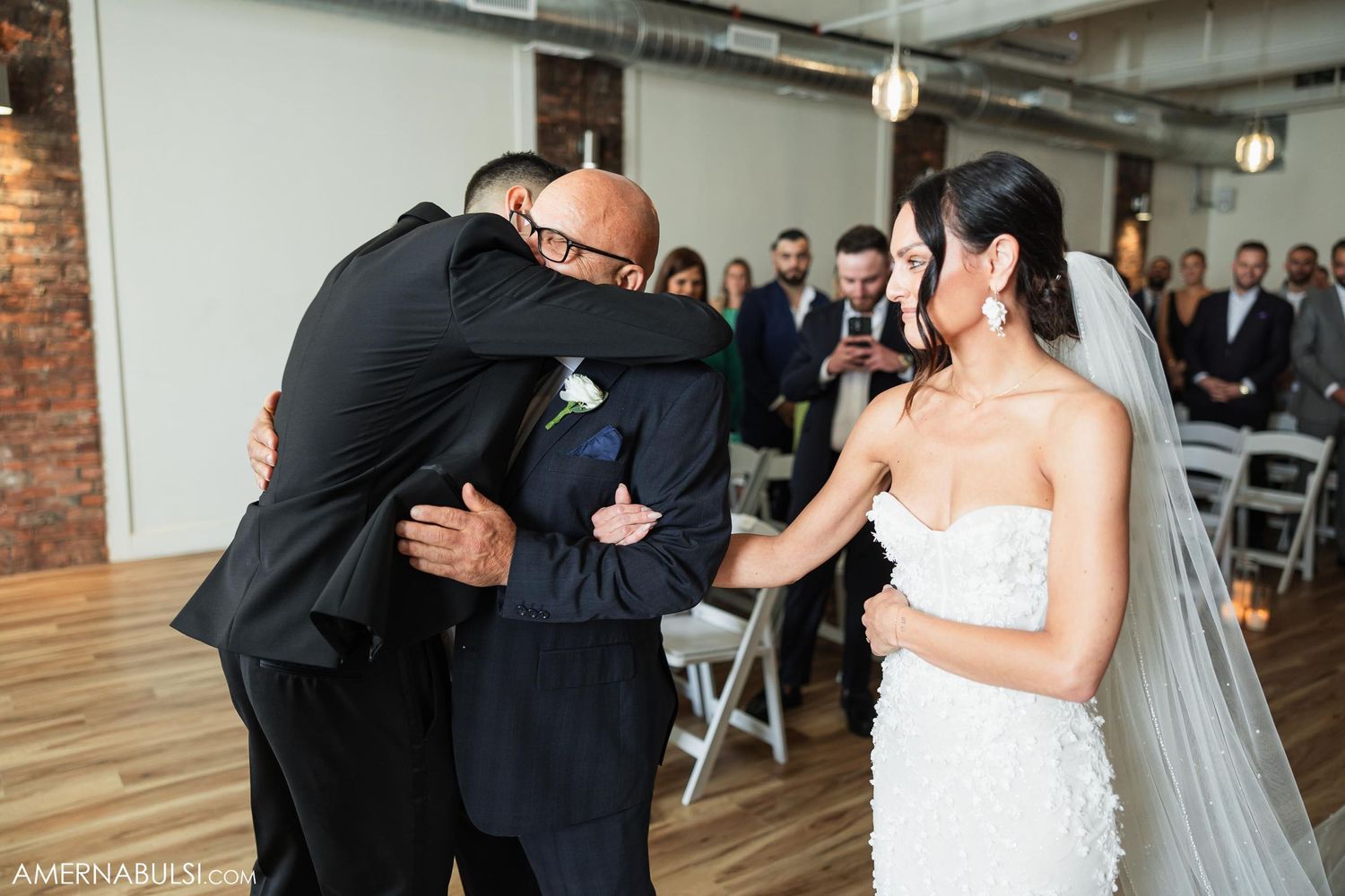 Emotional moment during wedding ceremony as family members embrace in an industrial-style venue.