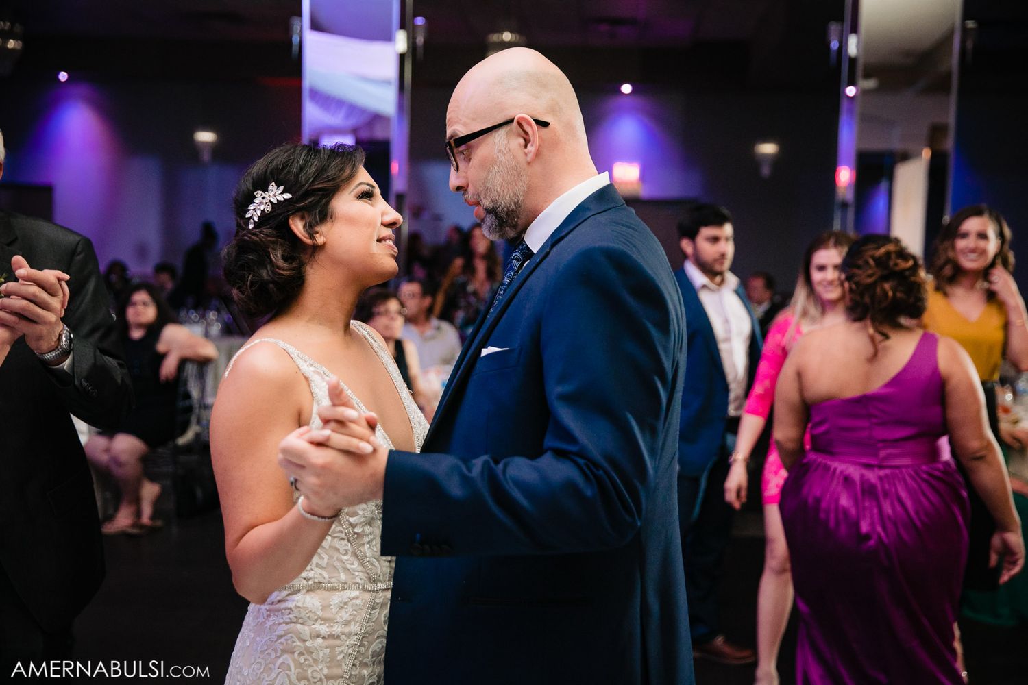 Wedding party dancing and celebrating in an indoor venue with purple ambient lighting.