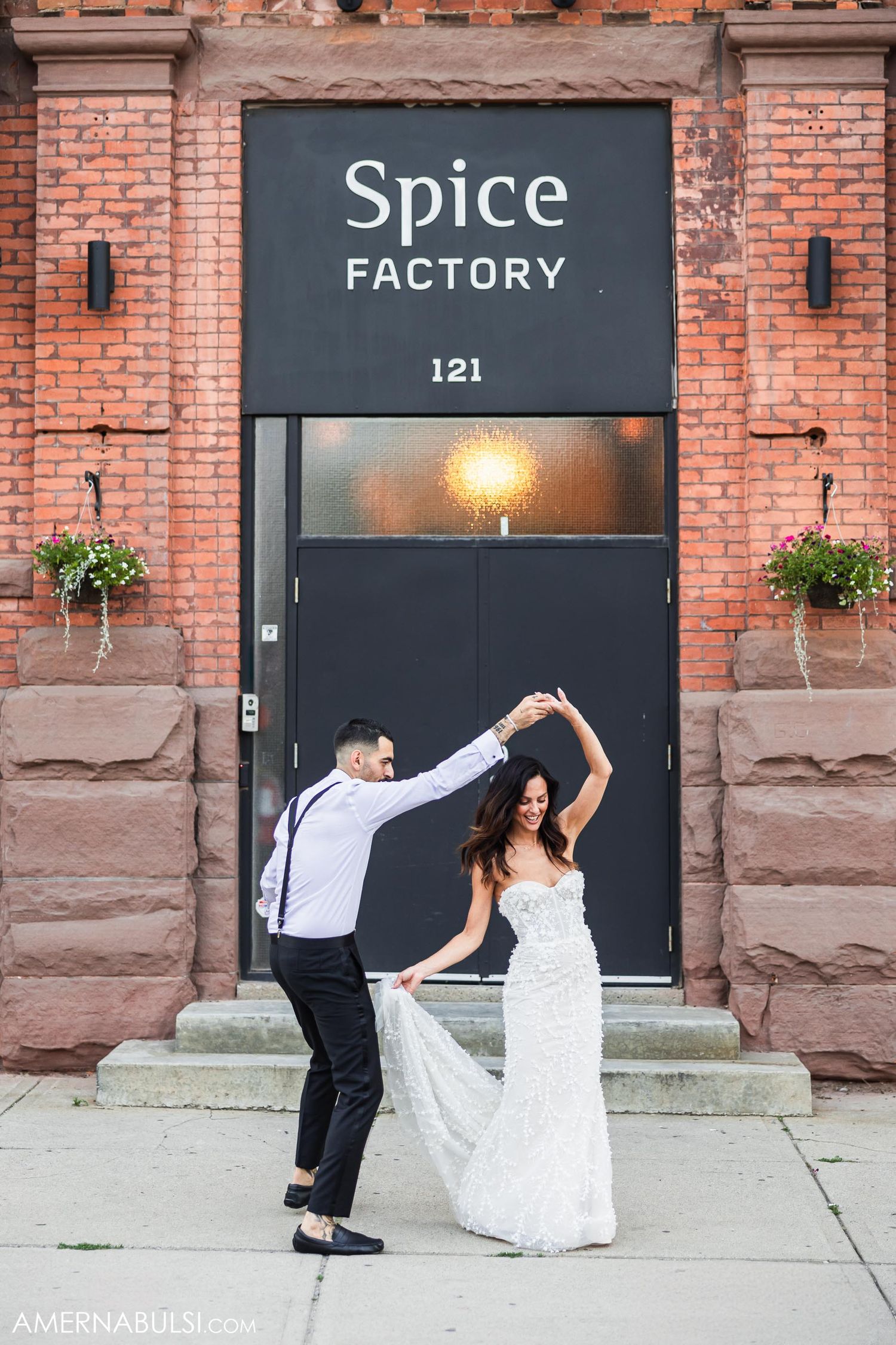Dancing couple in wedding attire in front of Spice Factory entrance with brick facade.