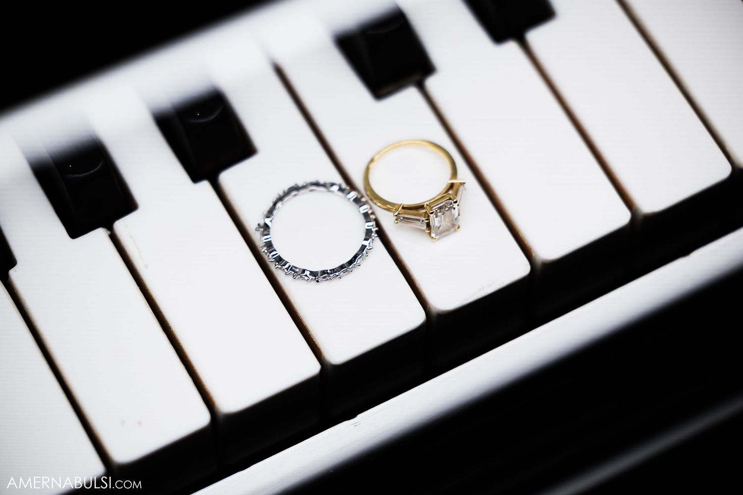 Wedding rings displayed artistically on white piano keys in dramatic lighting.