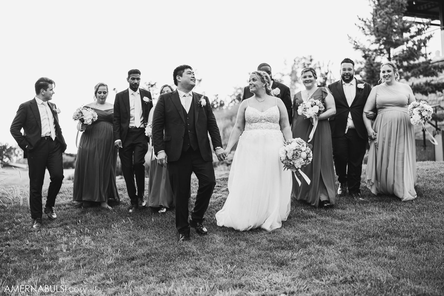 Wedding party walking and laughing together on a grassy hillside in black and white.