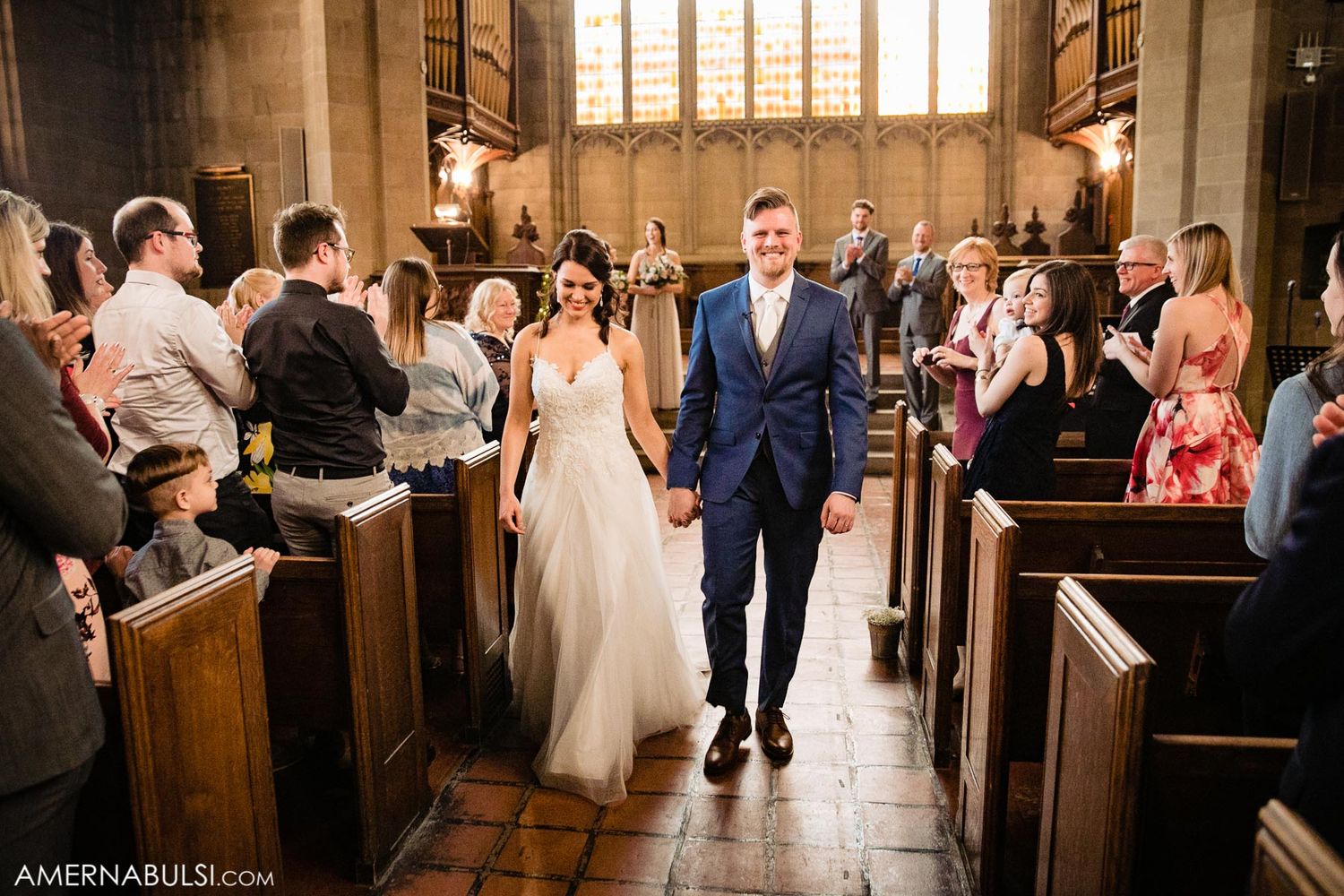 Wedding ceremony exit with guests lining church pews in historic stone chapel.