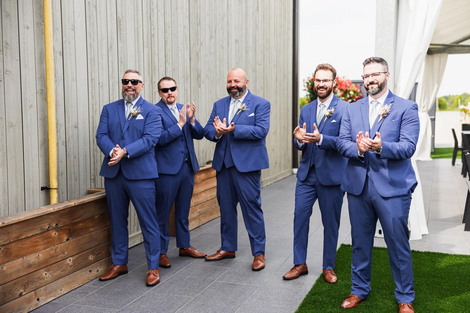 Groomsmen in coordinated navy blue suits pose casually against outdoor wall.