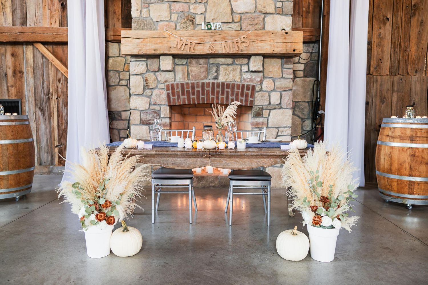 Rustic wedding reception setup with stone fireplace, wine barrels and autumn decor.