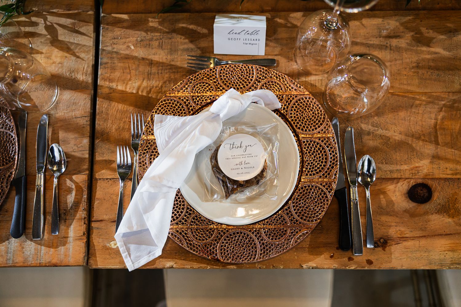 Elegant place settings with copper chargers and delicate glassware on wooden farmhouse tables.