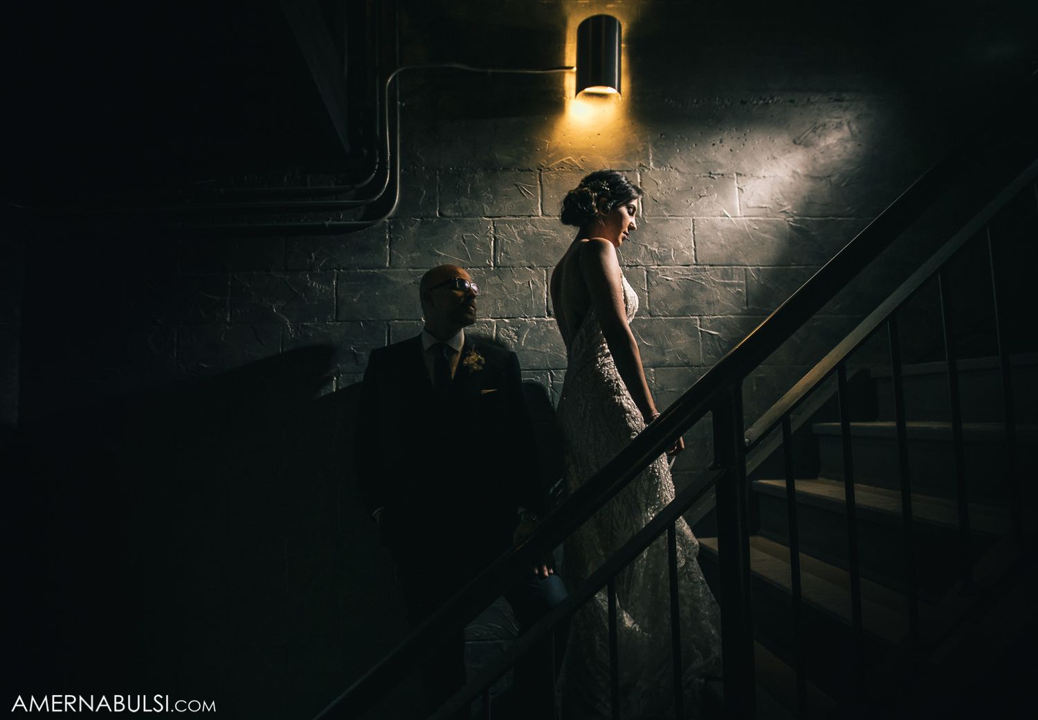 Dramatic black and white stairwell scene with moody lighting and brick walls creating atmospheric shadows.