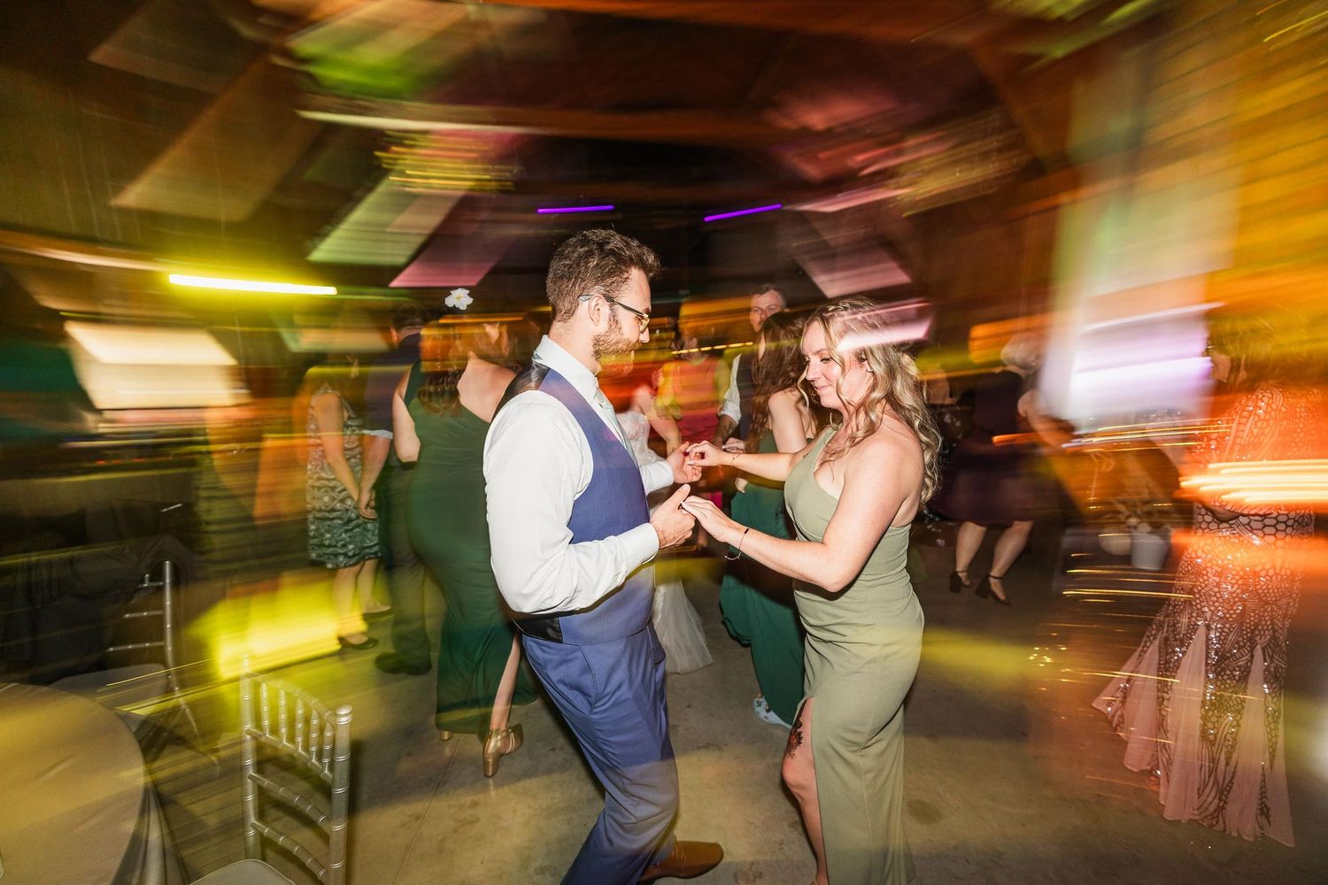 Couples dancing with motion blur effects under colorful party lighting at wedding reception.