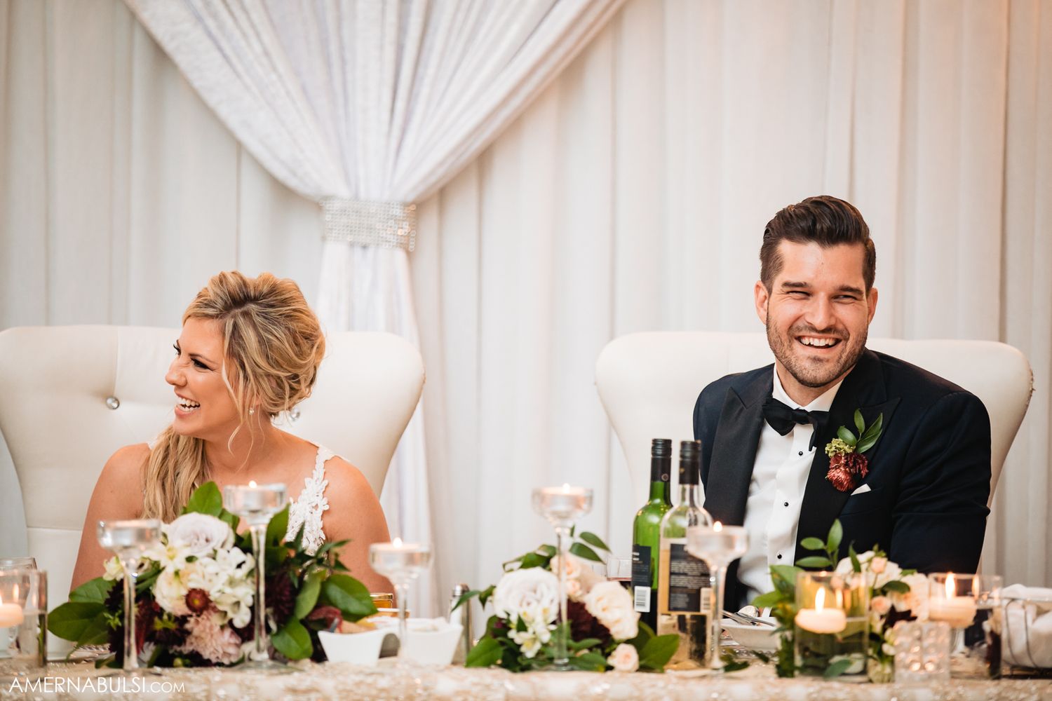 Wedding reception guests share joyful laughter during candid moments at an elegant white-draped venue.