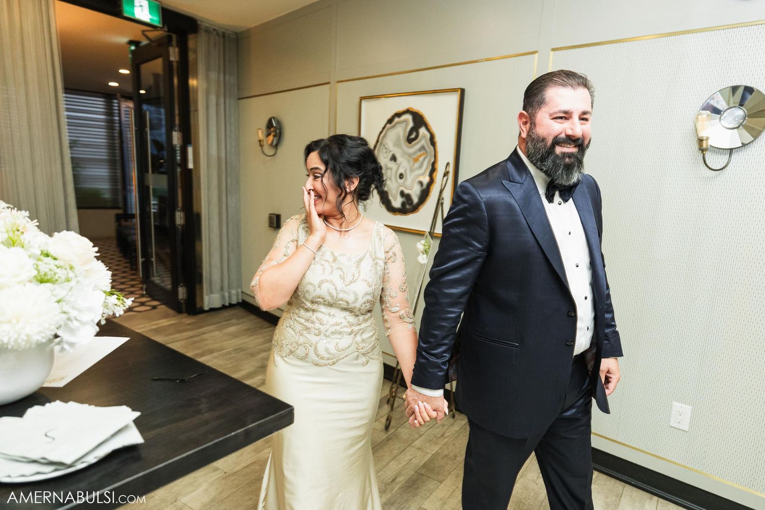 Wedding couple walks down a hallway with surprised expressions at an indoor venue.