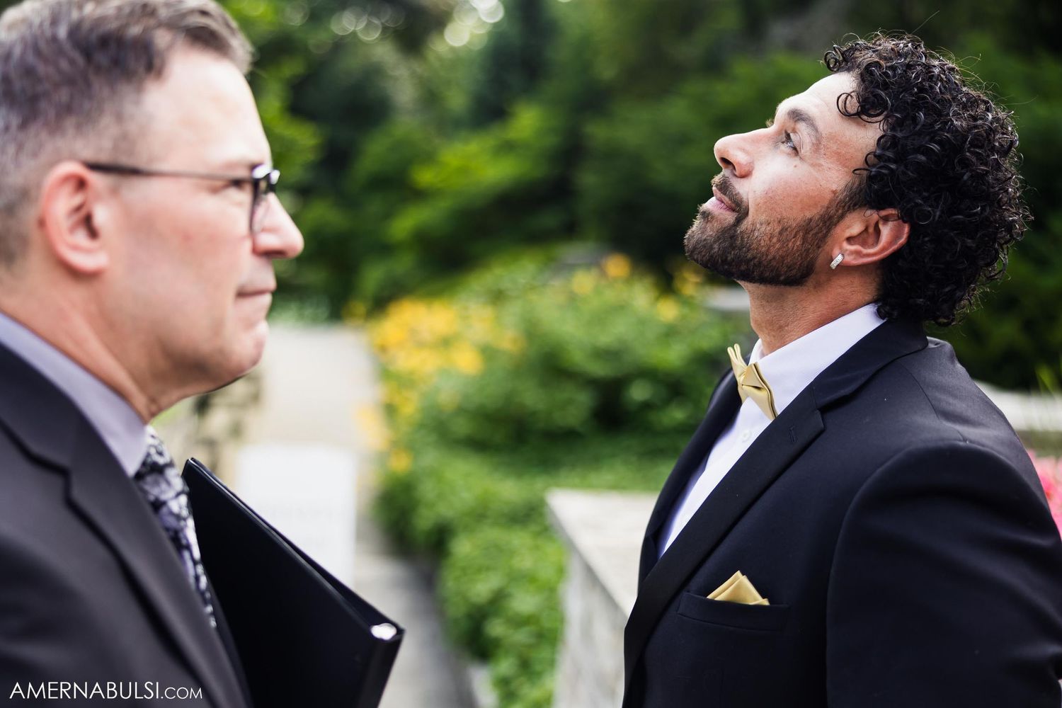 Two formally dressed figures sharing a candid moment in a garden setting.