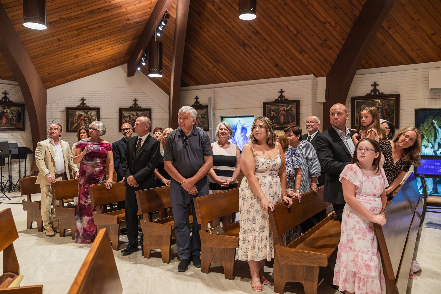 Guests standing in wooden pew church during wedding ceremony.