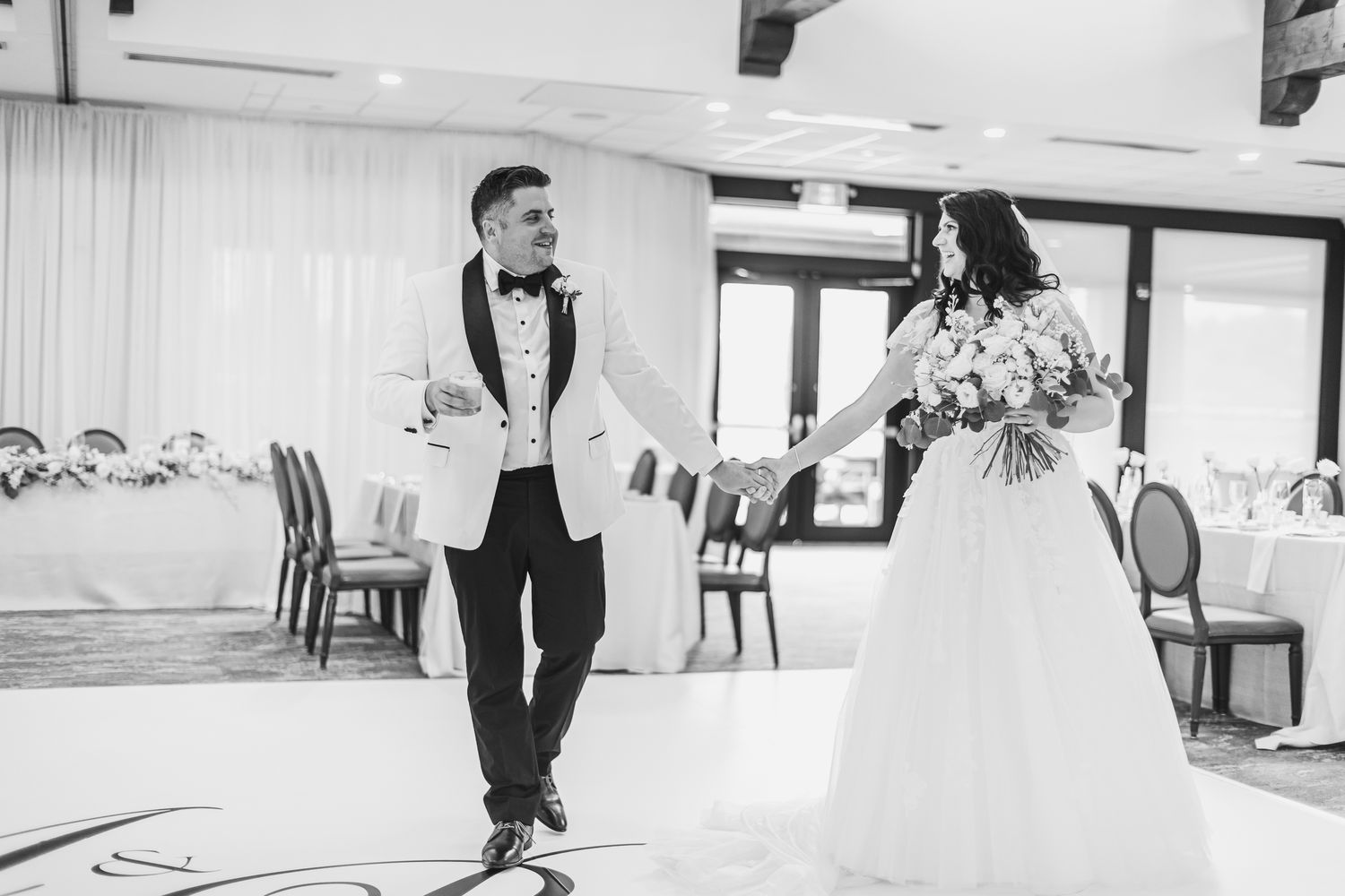 Black and white photo of a bride and groom entering their wedding reception hall, bride holding bouquet.