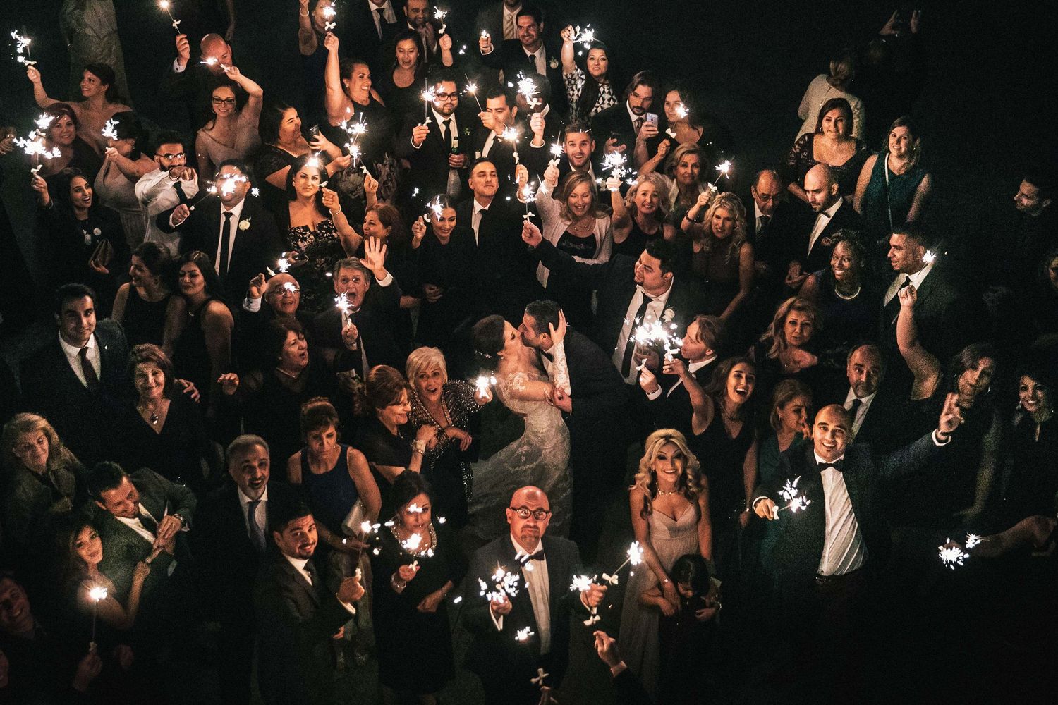 Large crowd of wedding guests raising their hands in celebration during an energetic reception party.