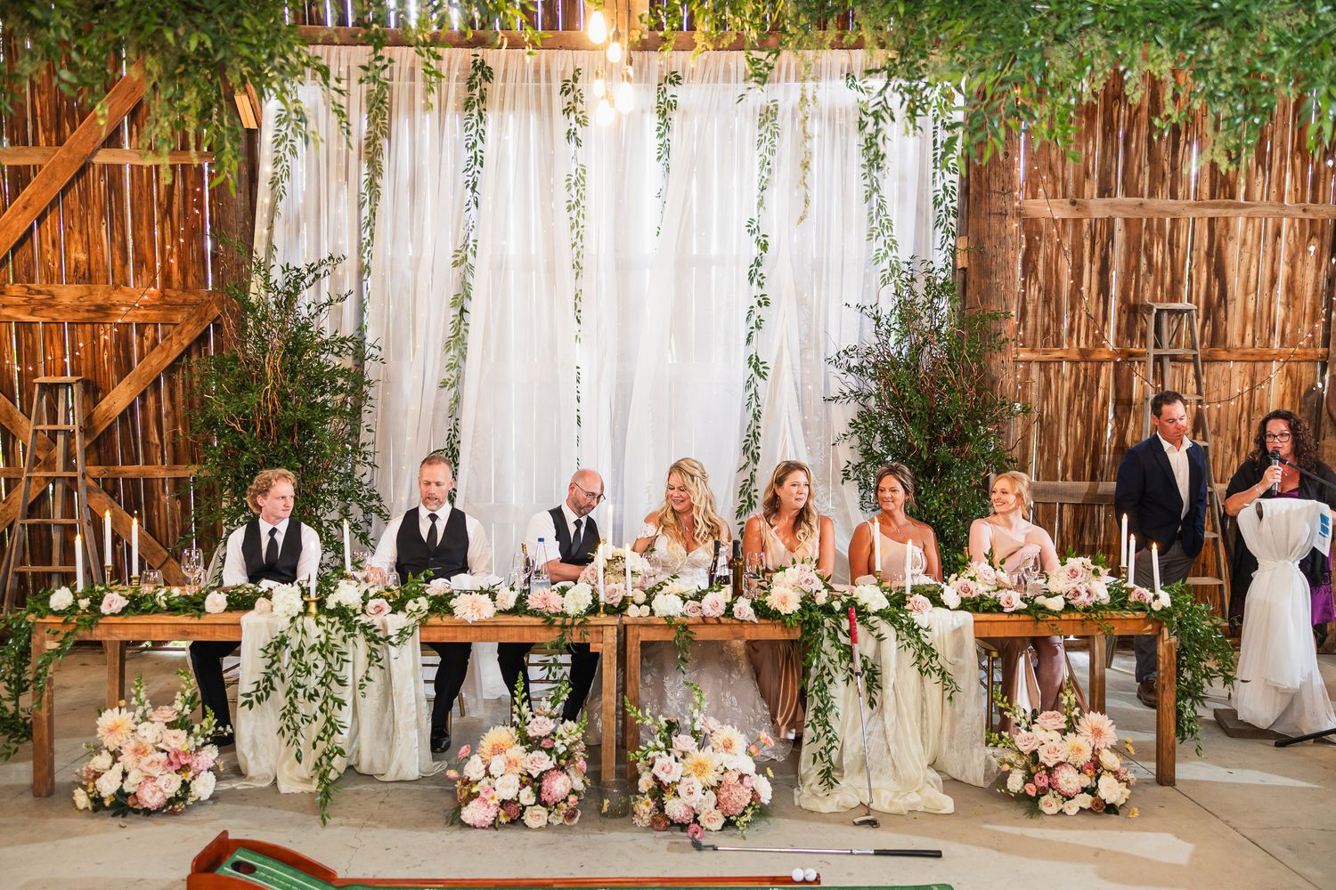 Long banquet tables adorned with floral centerpieces and greenery in a barn wedding reception.