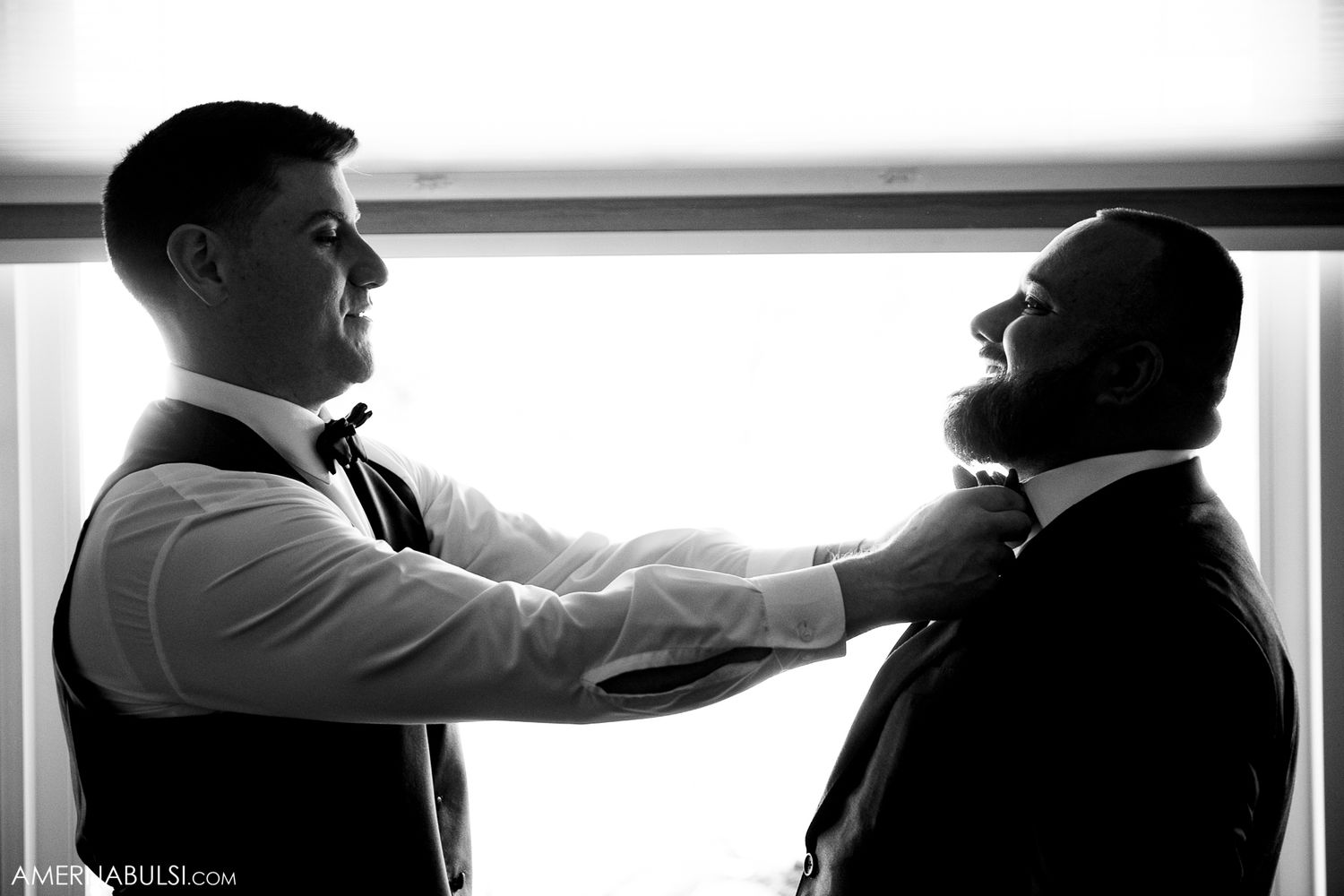 Silhouetted figures preparing formal attire near bright window in black and white photography.