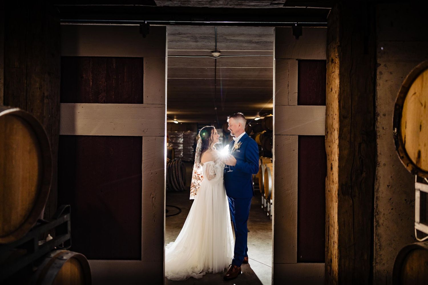 Wedding couple silhouetted in doorway between wine barrels.