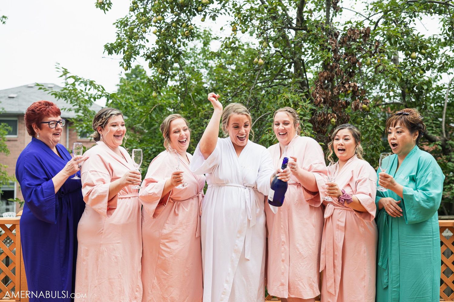Wedding party wearing robes in peach and turquoise colors celebrating together outdoors.