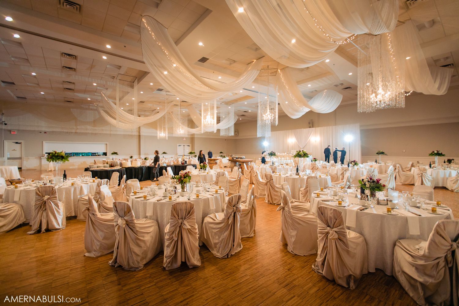 Elegant wedding reception ballroom with white draped decor and chair covers.