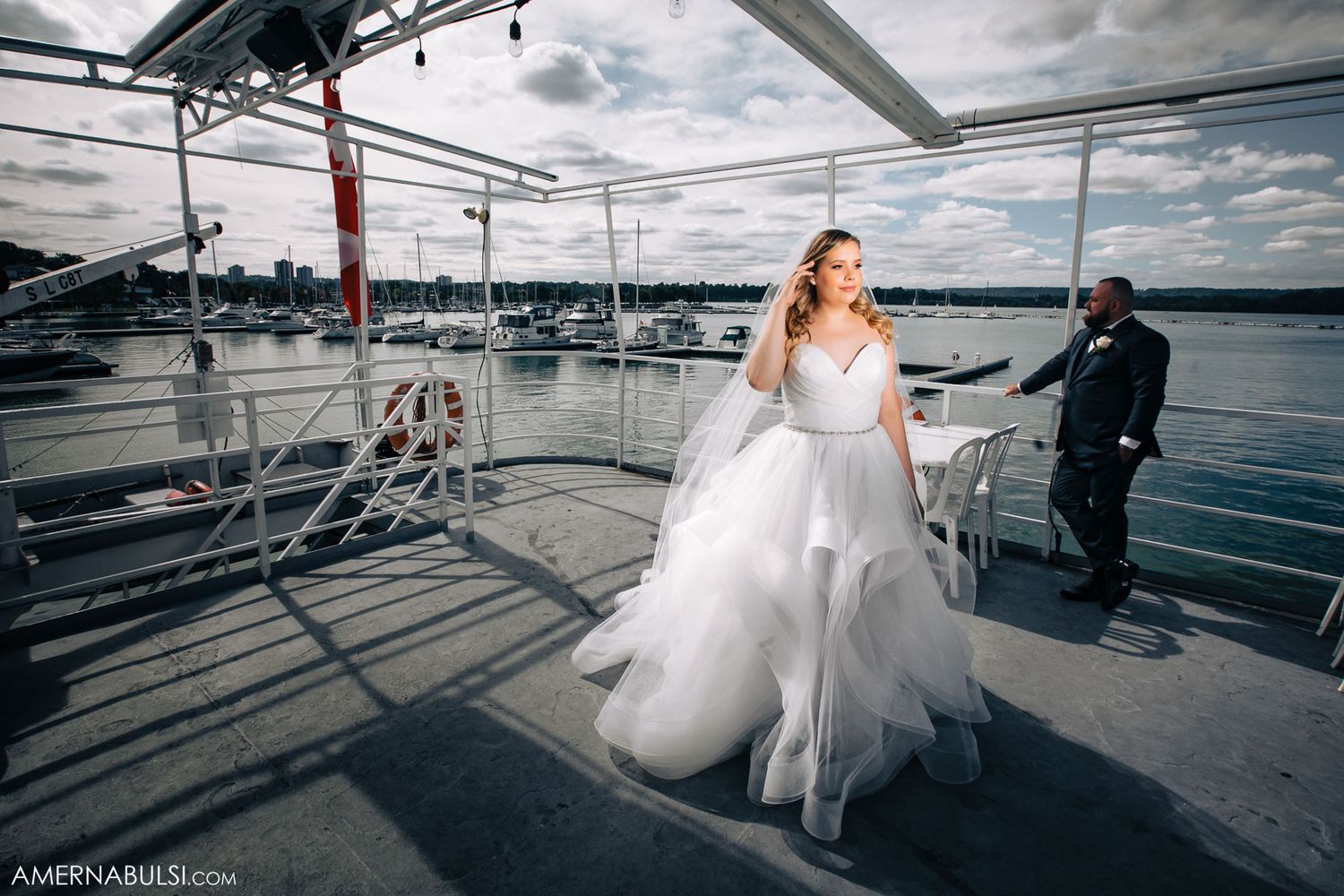 Wedding couple poses on a sailboat deck against scenic waterfront views during nautical photoshoot.