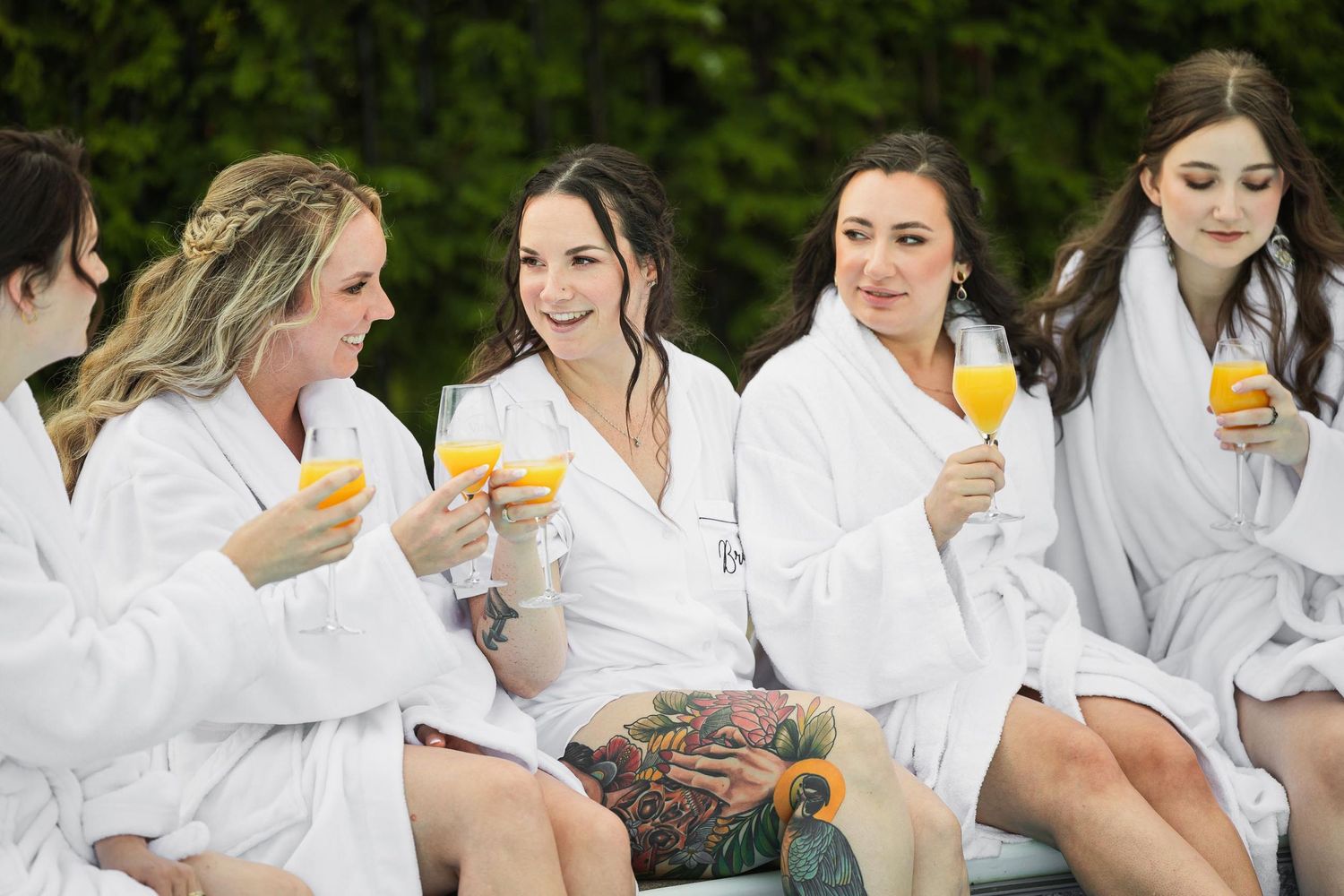 Group in white bathrobes enjoying mimosas together outdoors during a relaxing spa day.