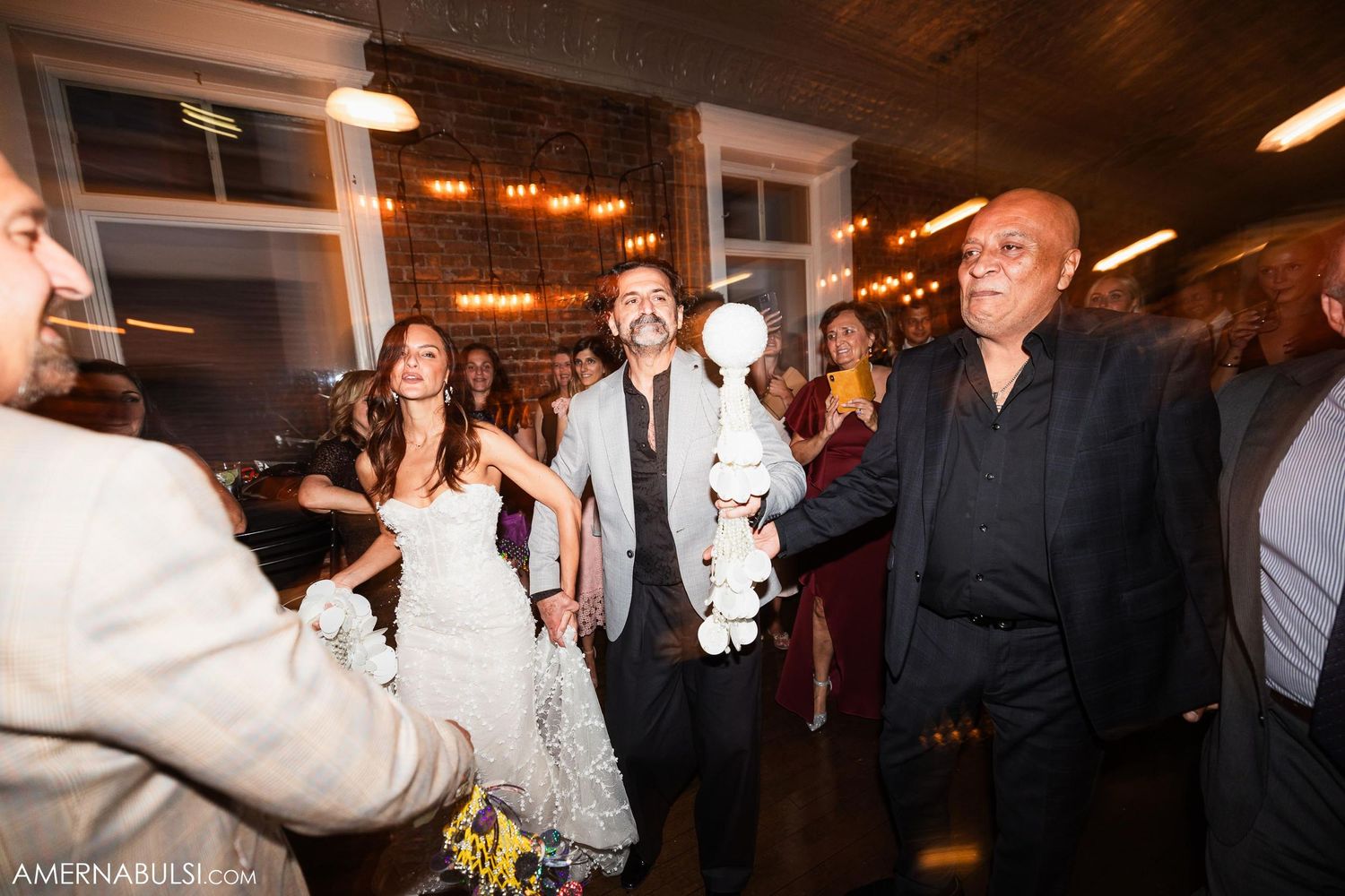 Wedding celebration with guests dancing and mingling under decorative lighting.
